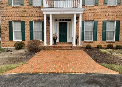 Front view of a brick house with green shutters, white columns, and a brick walkway leading to the door.