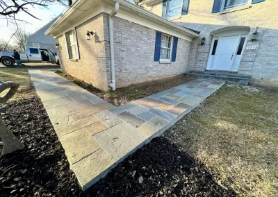 Stone walkway leading to the front door of a brick house, with a parked vehicle visible in the background.