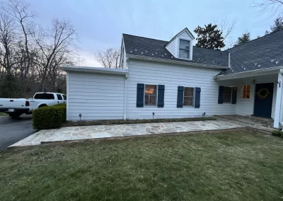 A white house with blue shutters, a stone walkway, and a grassy yard at dusk.