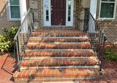 Brick steps with black metal railings leading to a maroon front door of a brick house.