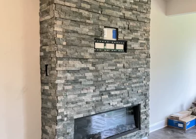A stone fireplace with a built-in TV mount and shelf, set against a white wall in a modern room.