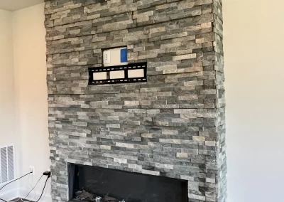 A stone fireplace with a TV mount and outlets above the firebox in a modern living room.
