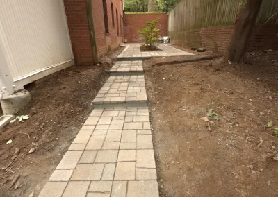 A newly constructed stone walkway runs between two brick buildings with bare soil on each side.