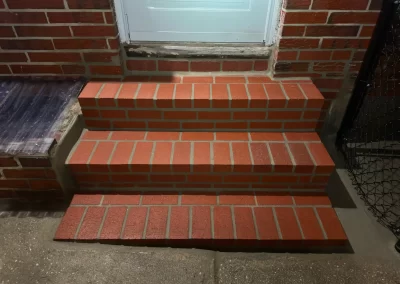Three red brick steps leading up to a white door, taken at night with a light shining from above.